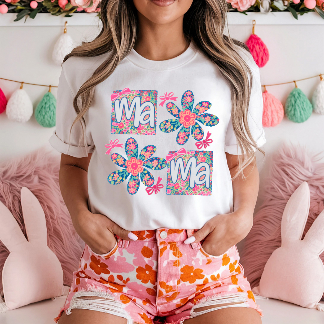 White graphic tee featuring colorful floral flowers and patchwork-style Mama lettering in pink, blue, and floral prints.