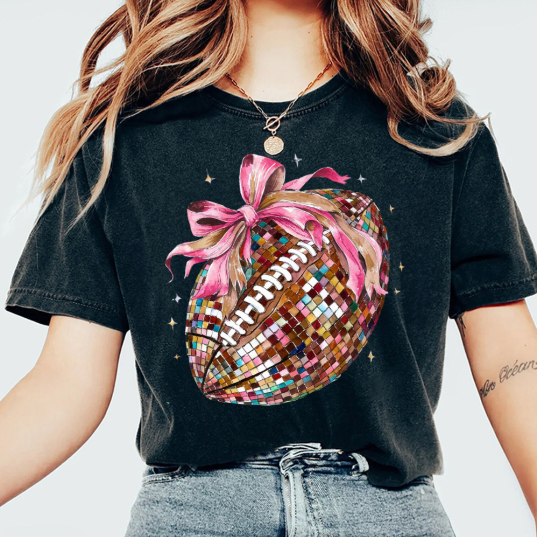 Black graphic tee featuring a mirrored disco football with a pink bow, perfect for football season and game day outfits.