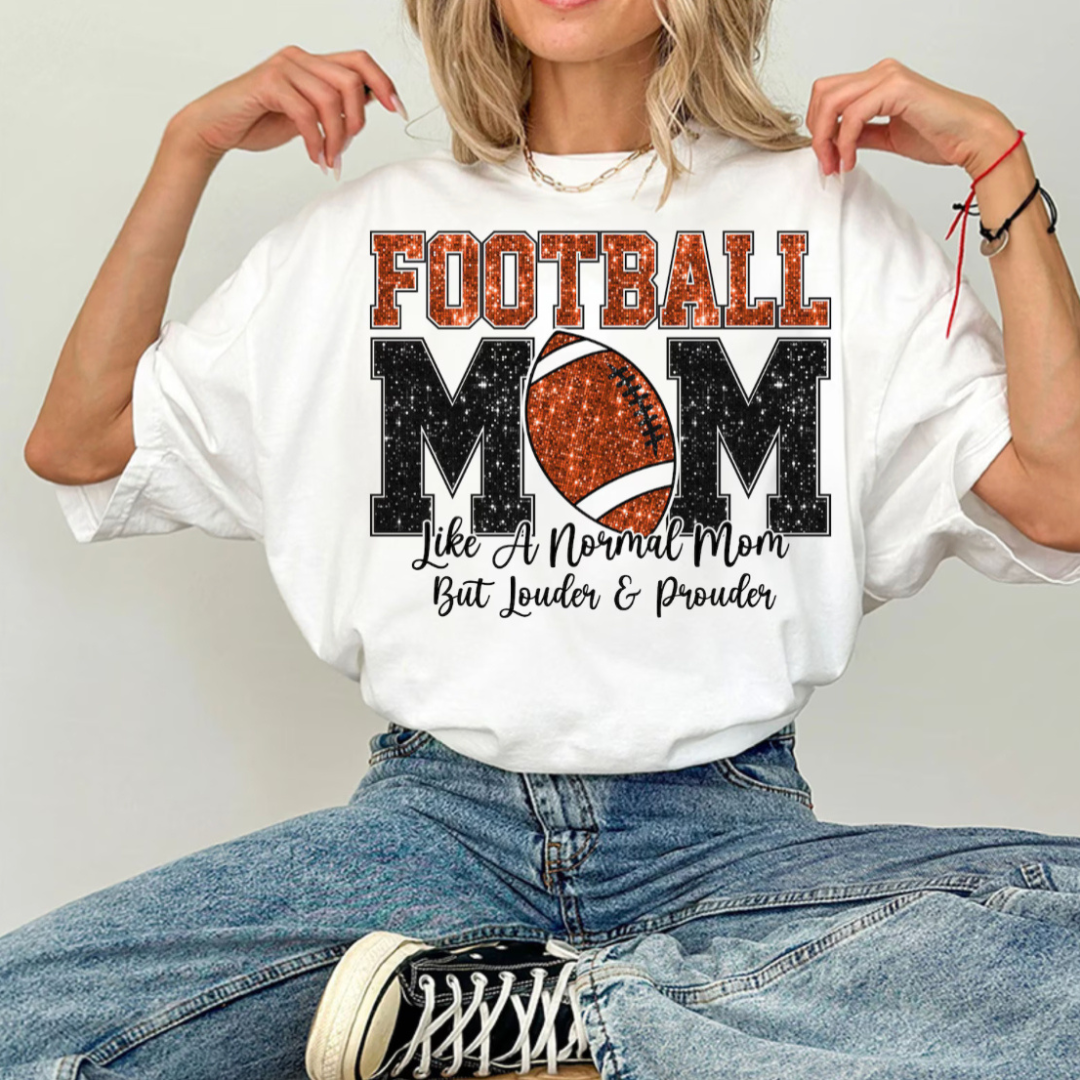 White graphic tee featuring a glitter-look "Football Mom" design with a football replacing the "O" and the phrase "Like A Normal Mom But Louder &amp; Prouder."