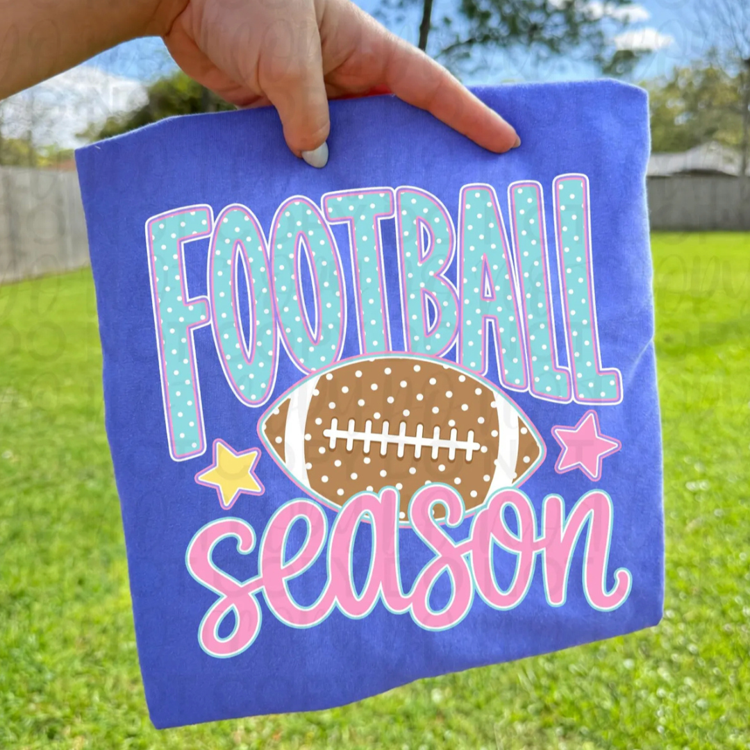 Royal blue graphic tee featuring aqua polka dot "Football" lettering, pink "Season" script, a football graphic, and pastel star accents.