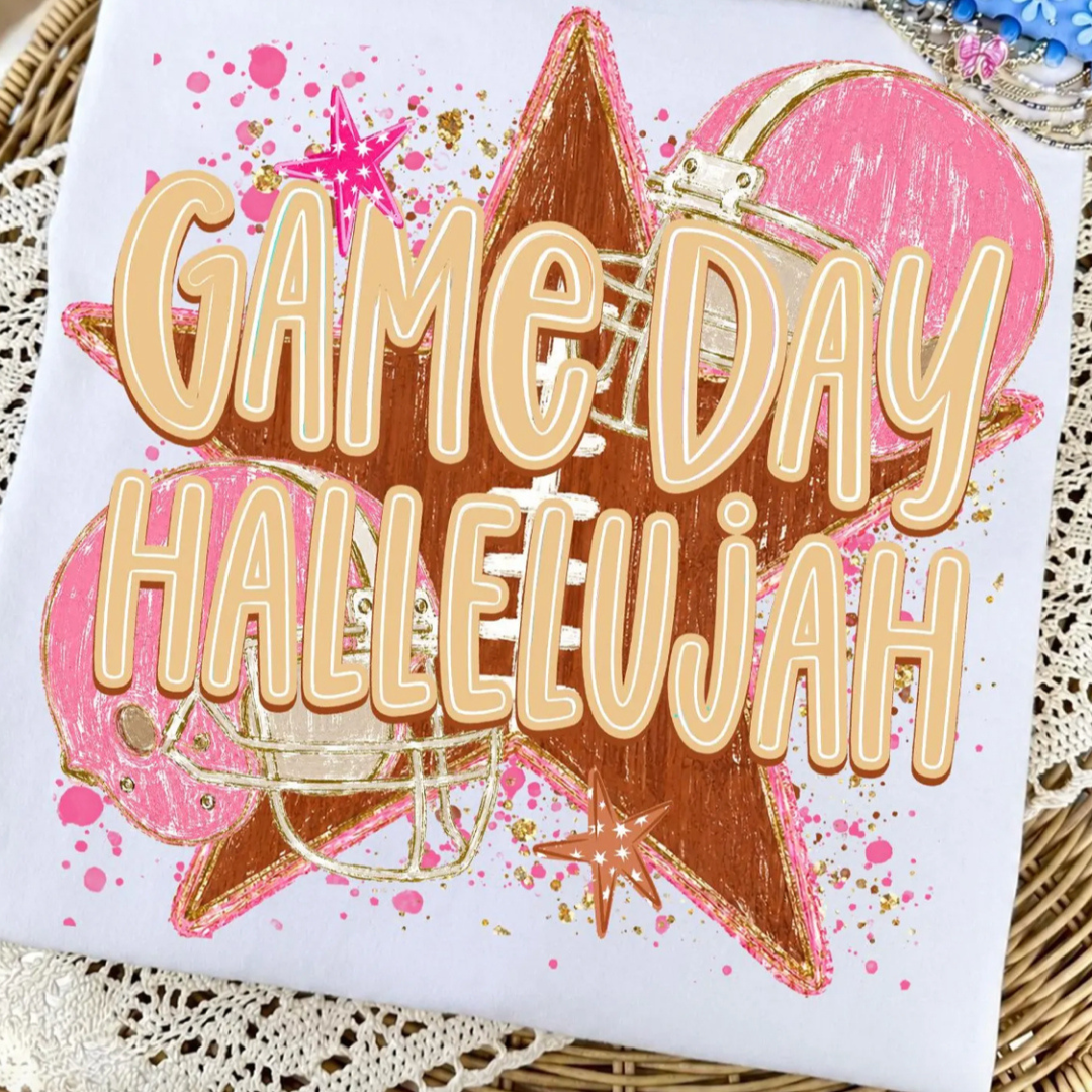 White graphic tee featuring "Game Day Hallelujah" with pink football helmets, a distressed football star, and football-themed accents.