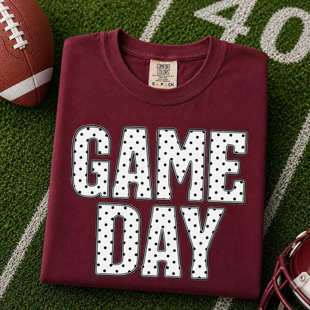Crimson graphic tee featuring oversized white "Game Day" lettering with a black polka dot pattern.