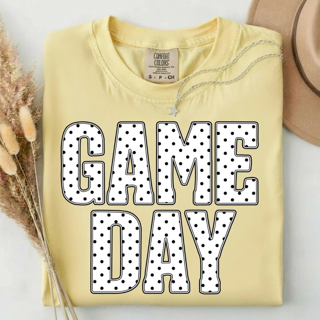 Butter yellow graphic tee featuring oversized white "Game Day" lettering with a black polka dot pattern.