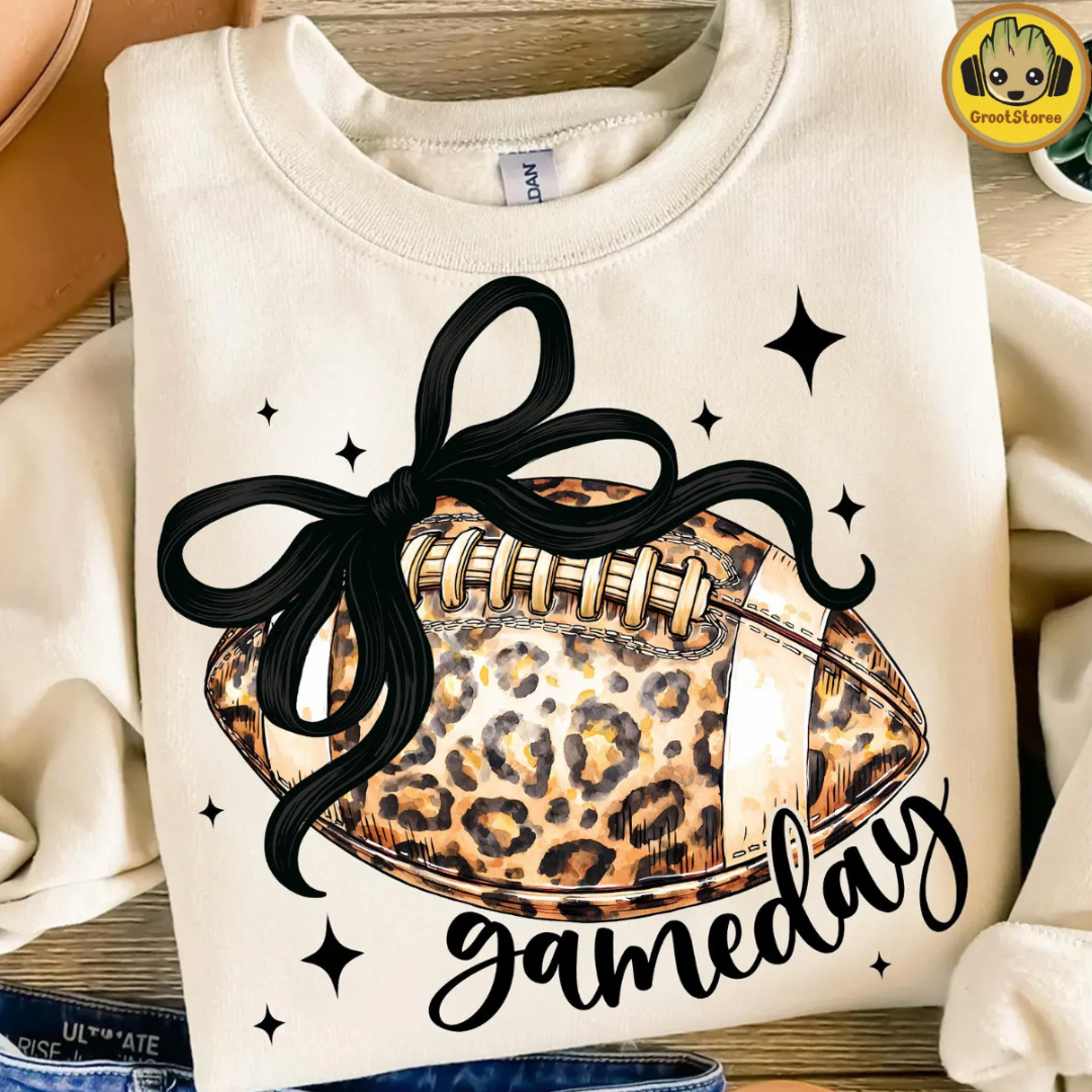 Natural graphic tee featuring a leopard print football with a large black bow and "gamedays" script.