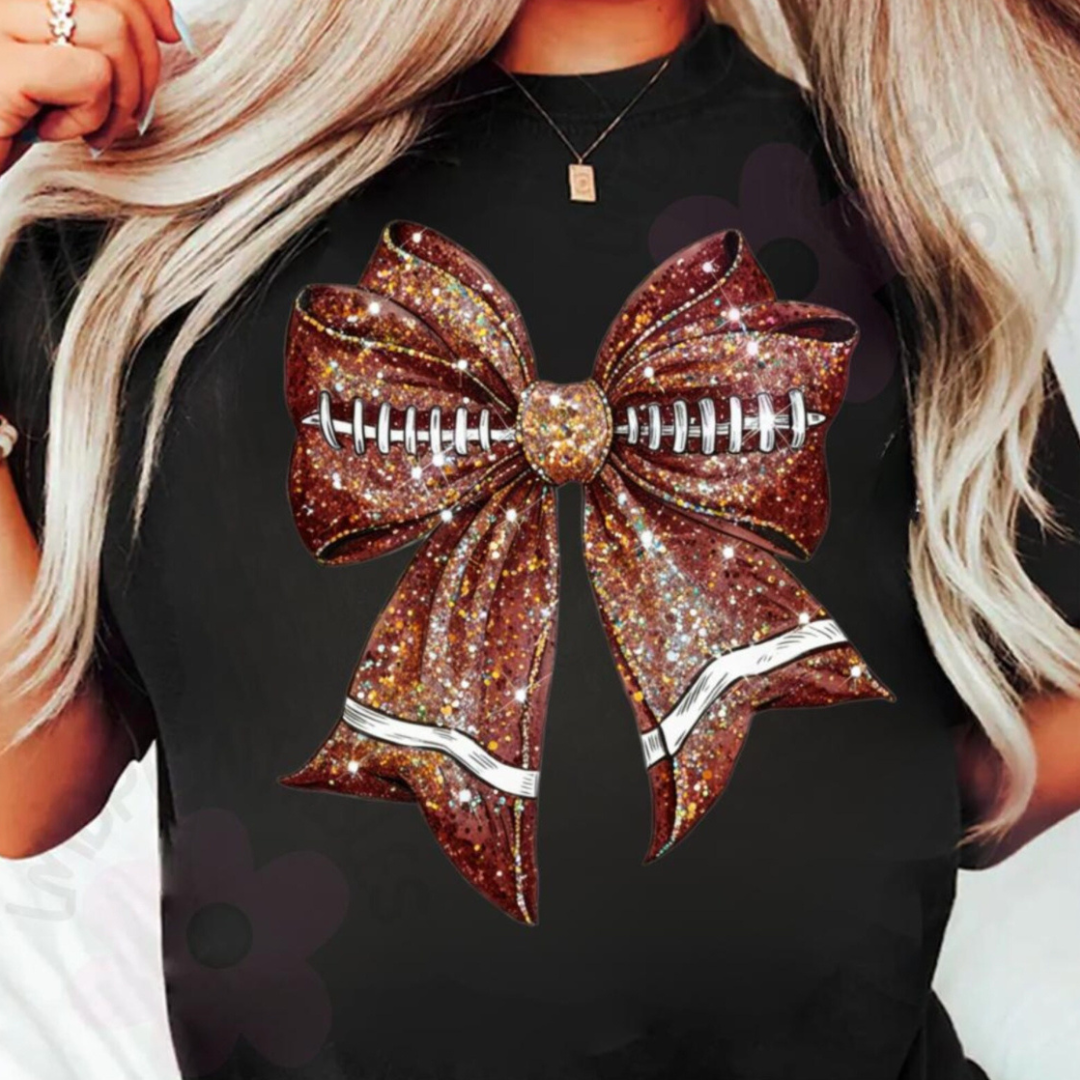 Black graphic tee featuring a glitter-inspired brown football bow with football laces through the center, perfect for football season and game day.