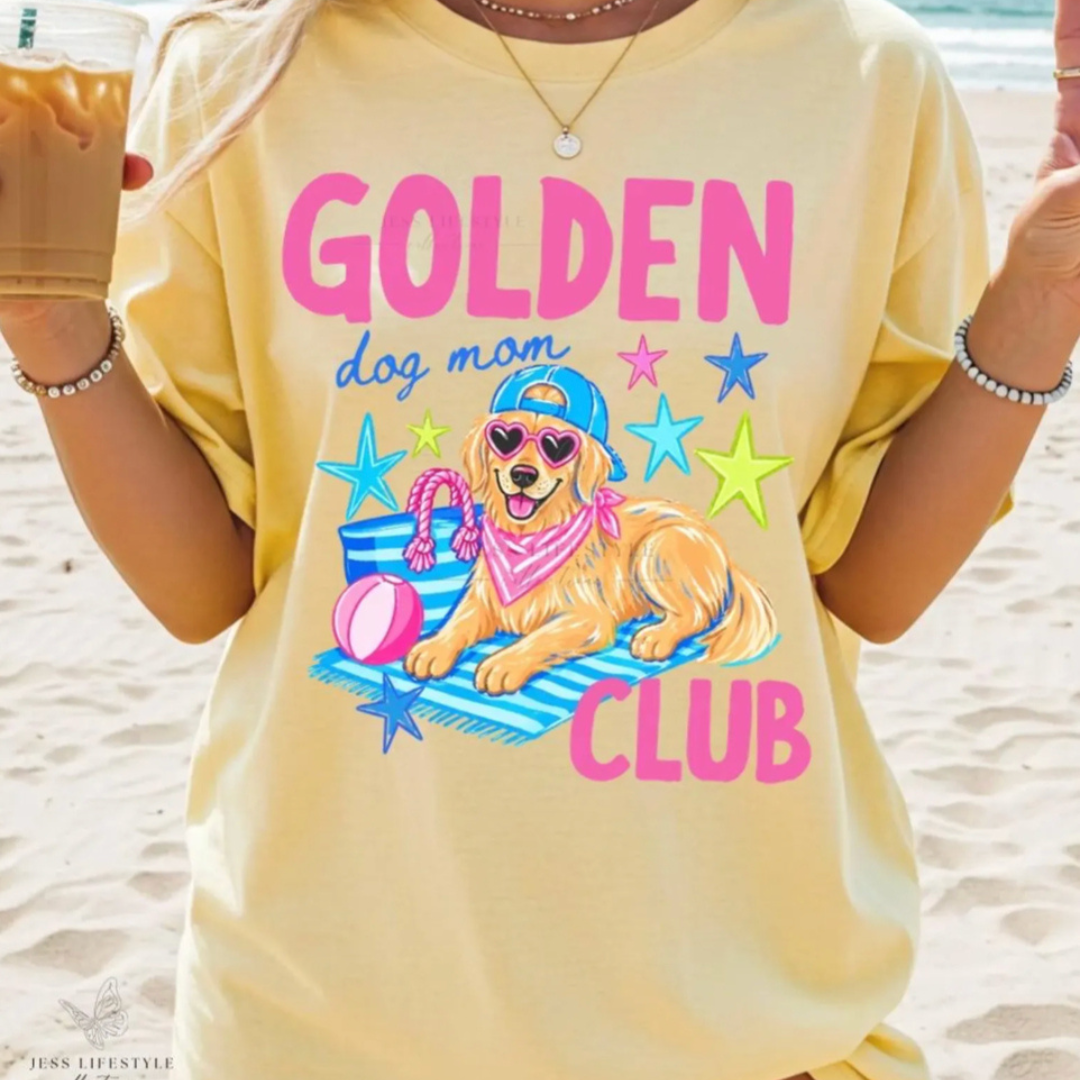 Butter yellow graphic tee featuring a Golden Retriever wearing heart sunglasses, a cap, and a pink bandana with colorful "Golden Dog Mom Club" lettering and beach-themed artwork.