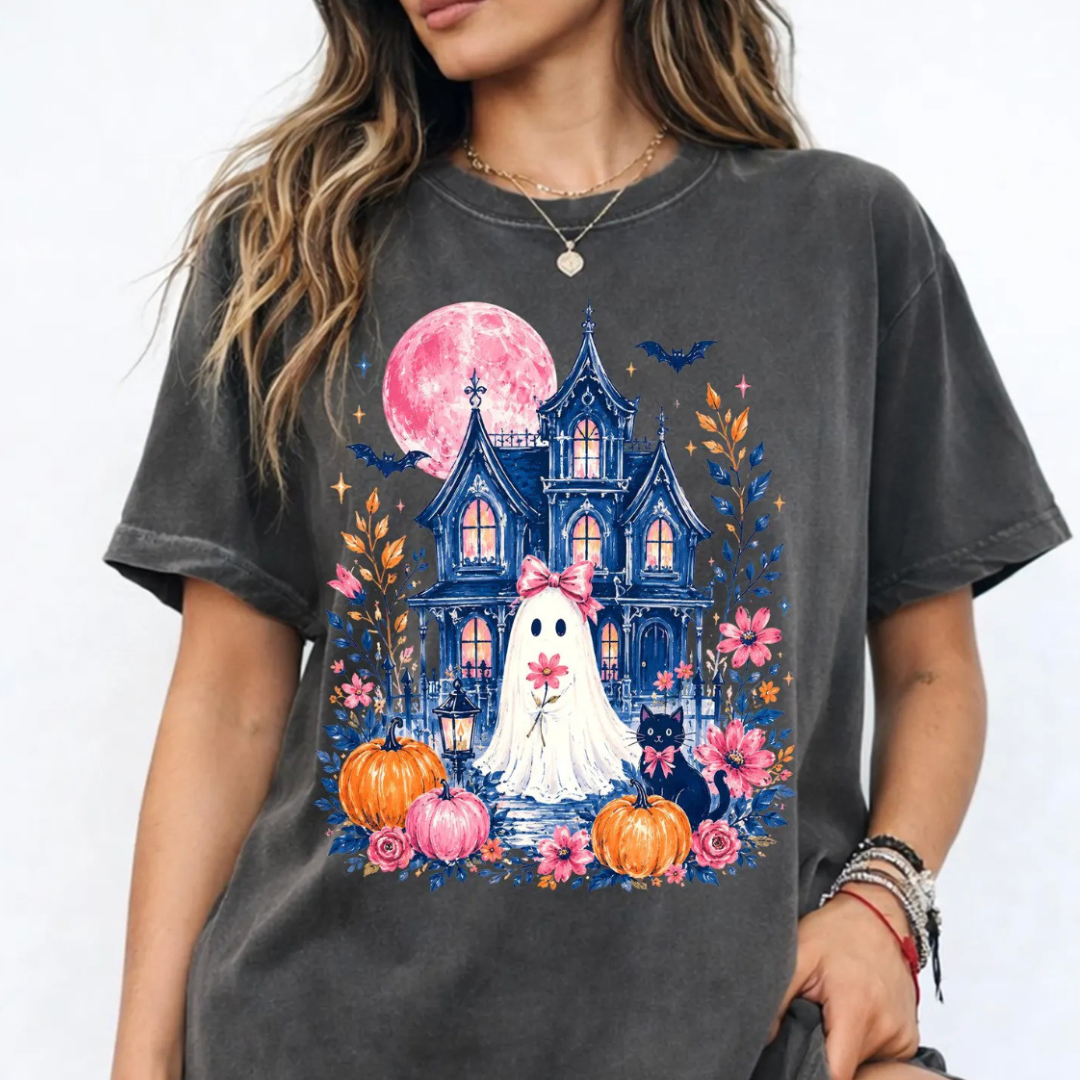 Pepper Comfort Colors graphic tee featuring a ghost with a pink bow standing in front of a haunted Victorian house with a pink moon, pumpkins, florals, bats, and a black cat.