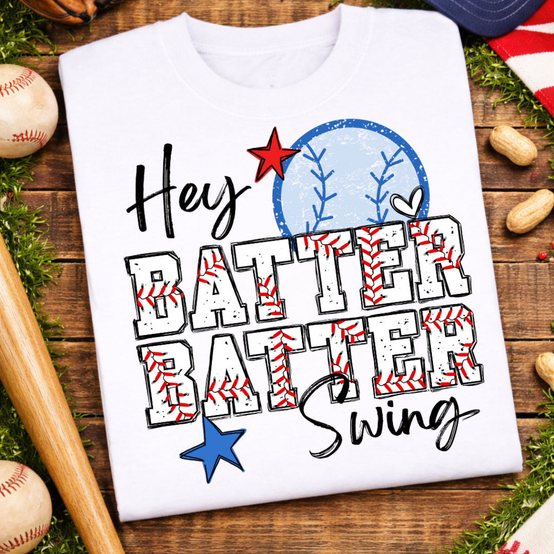 White graphic tee featuring the phrase "Hey Batter Batter Swing" with baseball stitching, stars, and red, white, and blue baseball graphics.