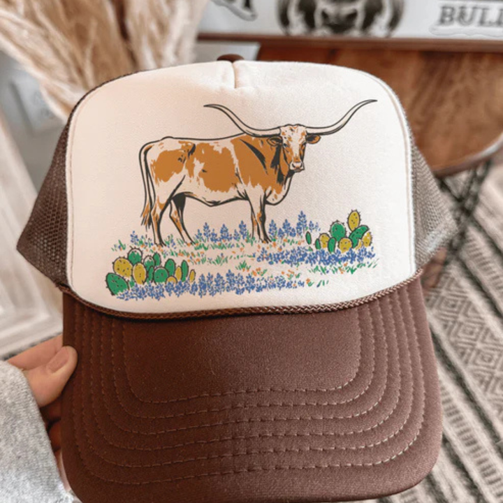 Brown and white trucker hat with a longhorn cow design on a neutral background