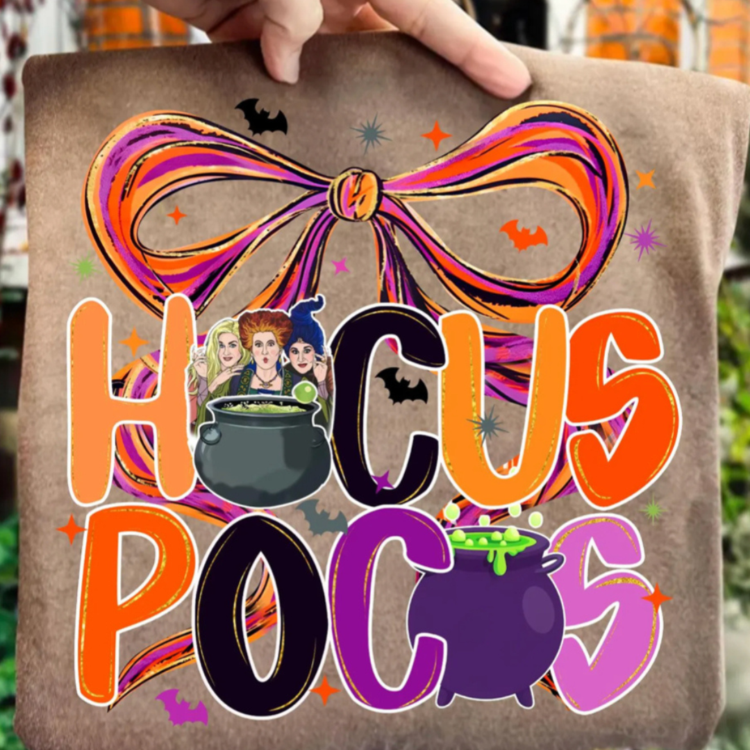 Mocha brown Halloween graphic tee featuring colorful "Hocus Pocus" lettering with an oversized bow, bubbling cauldrons, bats, and whimsical Halloween accents.
