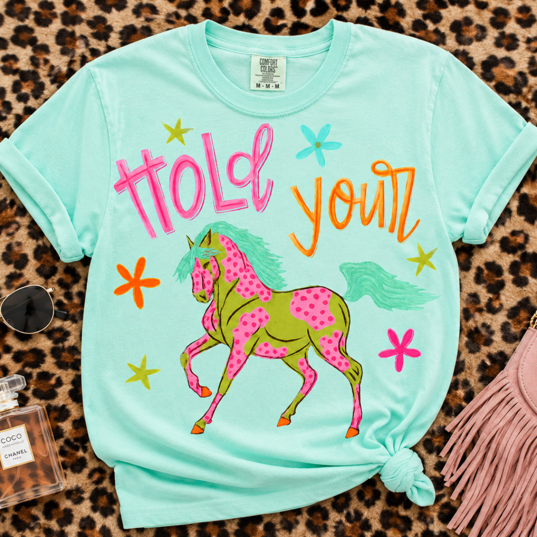 Mint green Comfort Colors graphic tee featuring a colorful spotted horse with Hold Your lettering and bright western-inspired artwork.