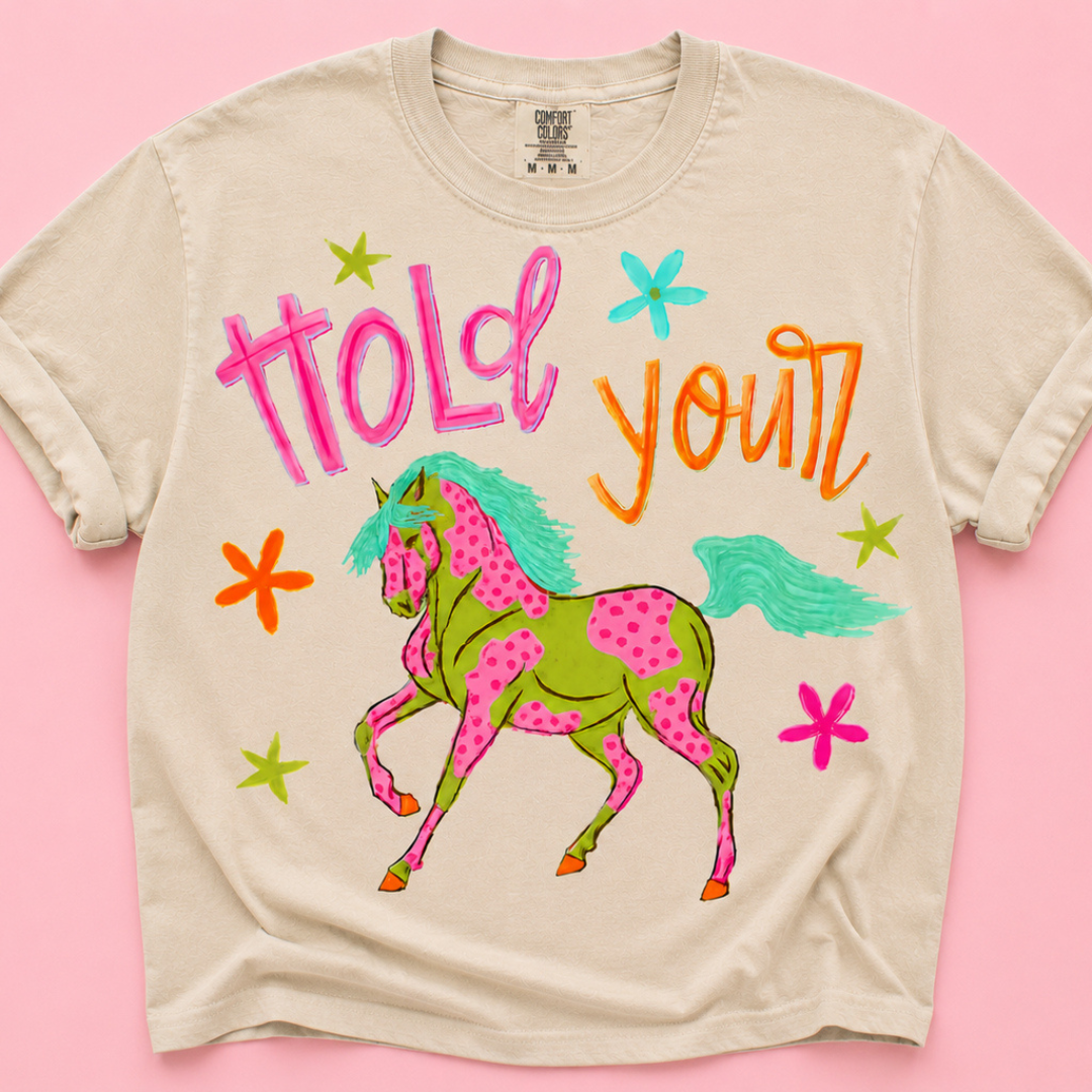 Natural beige graphic tee featuring a colorful spotted horse graphic with Hold Your wording and bright western-inspired artwork.