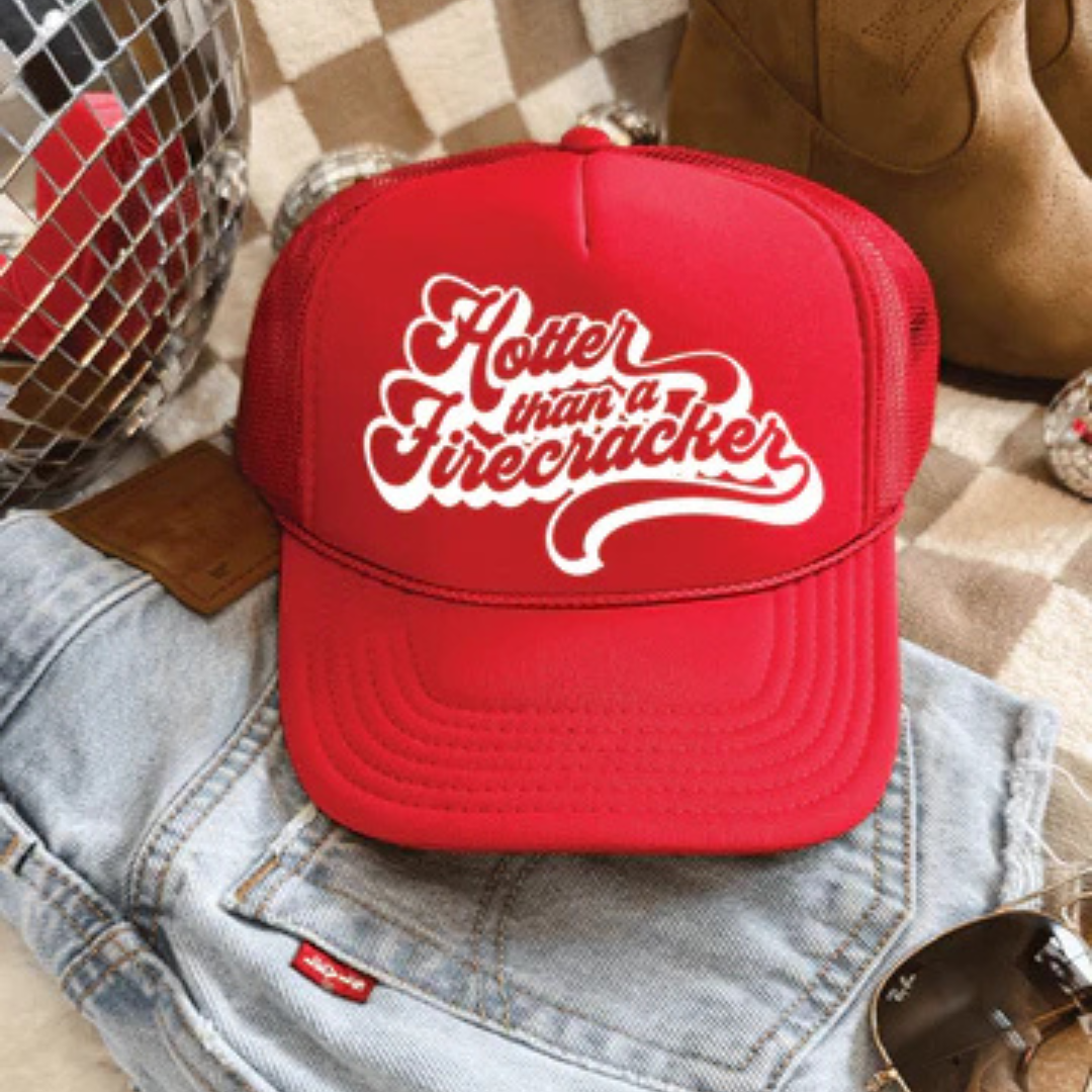 Red foam trucker hat featuring Hotter Than a Firecracker retro script graphic with mesh back and adjustable snapback closure.