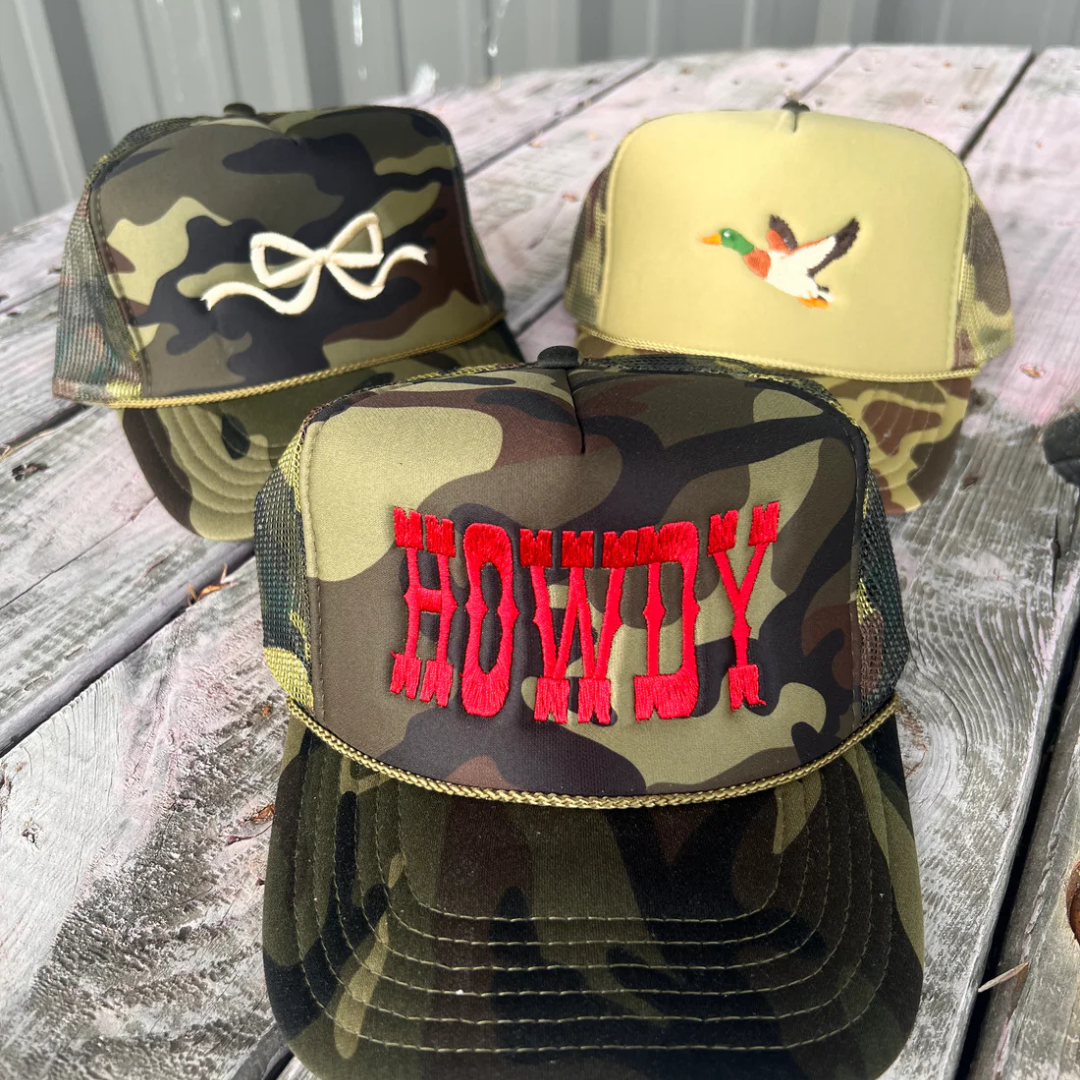 Camouflage trucker hat featuring bold red embroidered Howdy lettering with an adjustable mesh back.