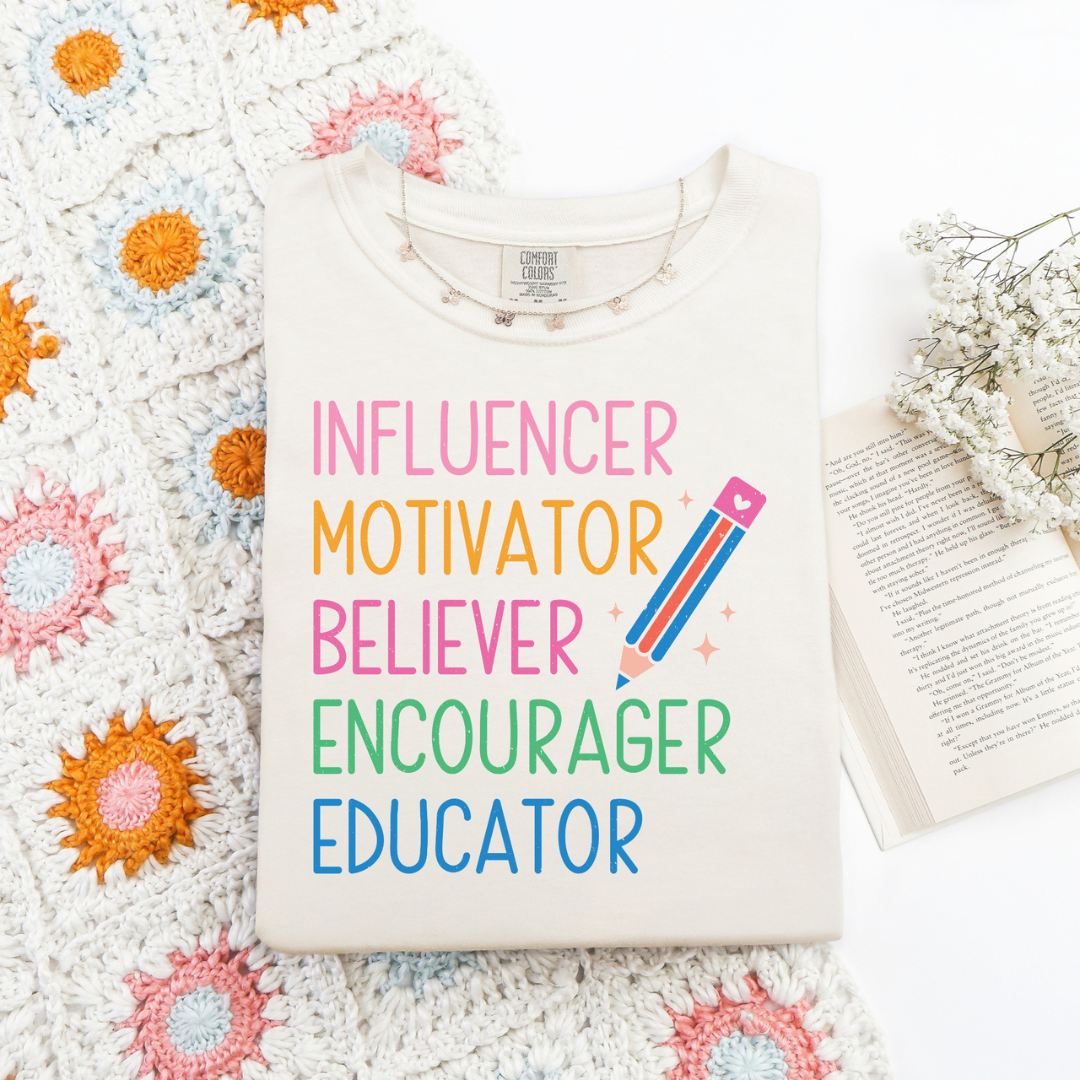 Ivory teacher graphic tee featuring colorful words "Influencer, Motivator, Believer, Encourager, Educator" with a multicolor pencil.