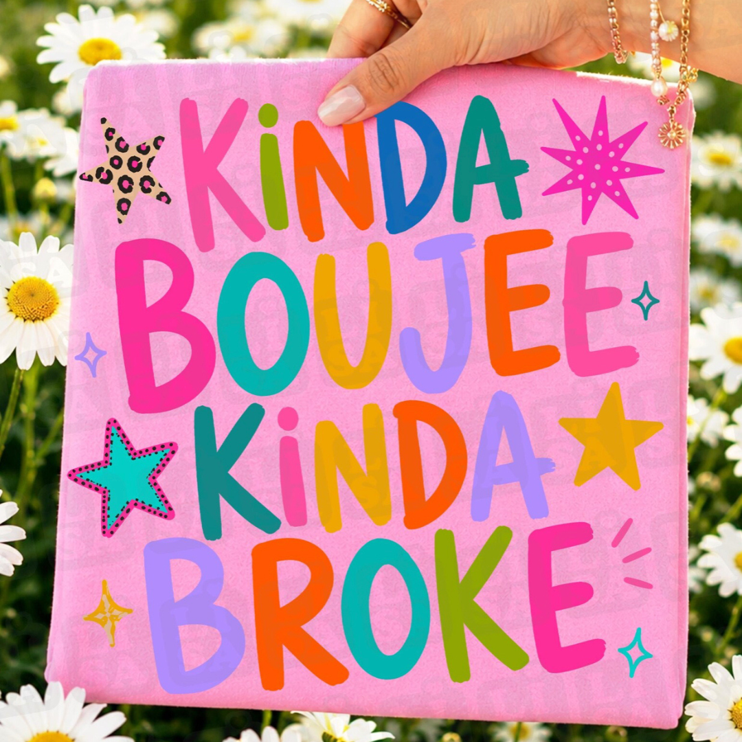 Pink graphic tee featuring colorful retro lettering that reads "Kinda Boujee Kinda Broke" with bright star accents.