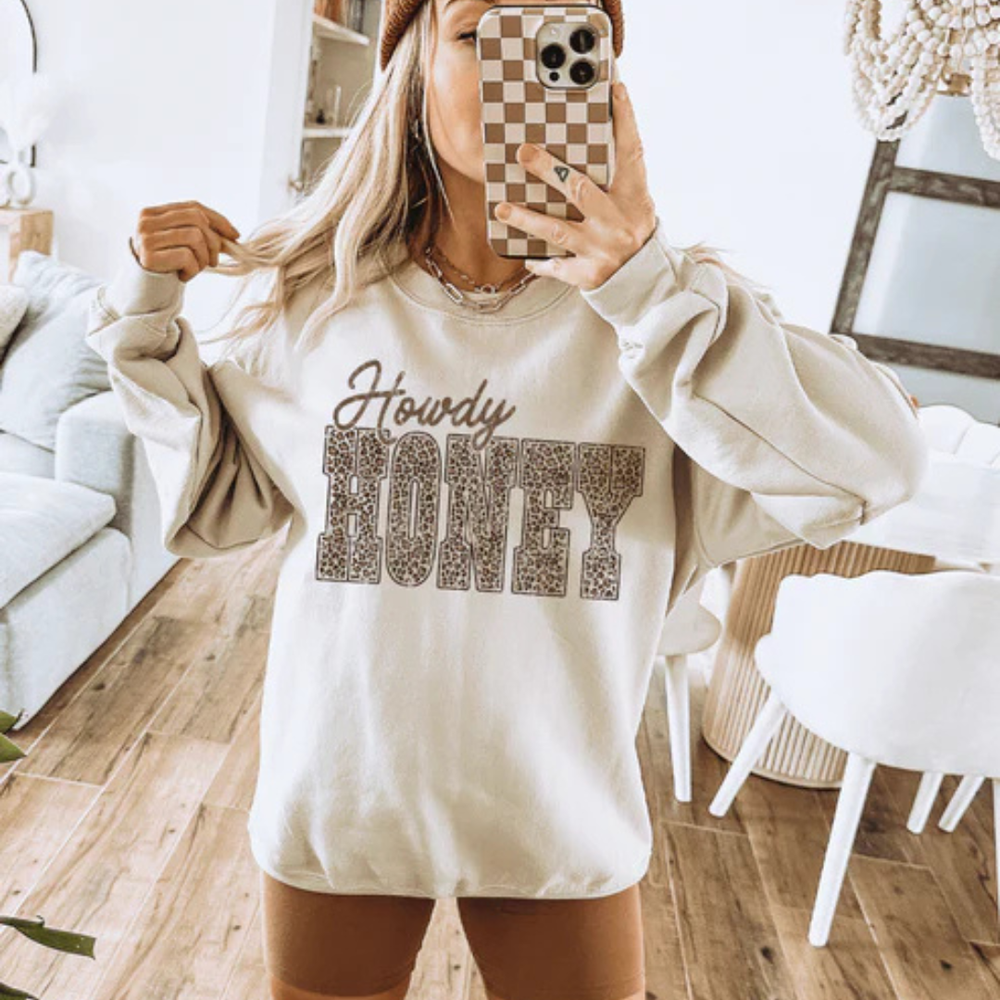 Cream graphic tee and sweatshirt featuring a Howdy Honey design with bold leopard print lettering.