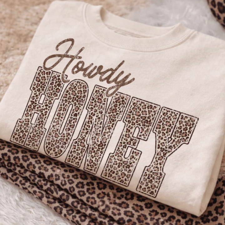 Cream graphic tee and sweatshirt featuring a Howdy Honey design with bold leopard print lettering.