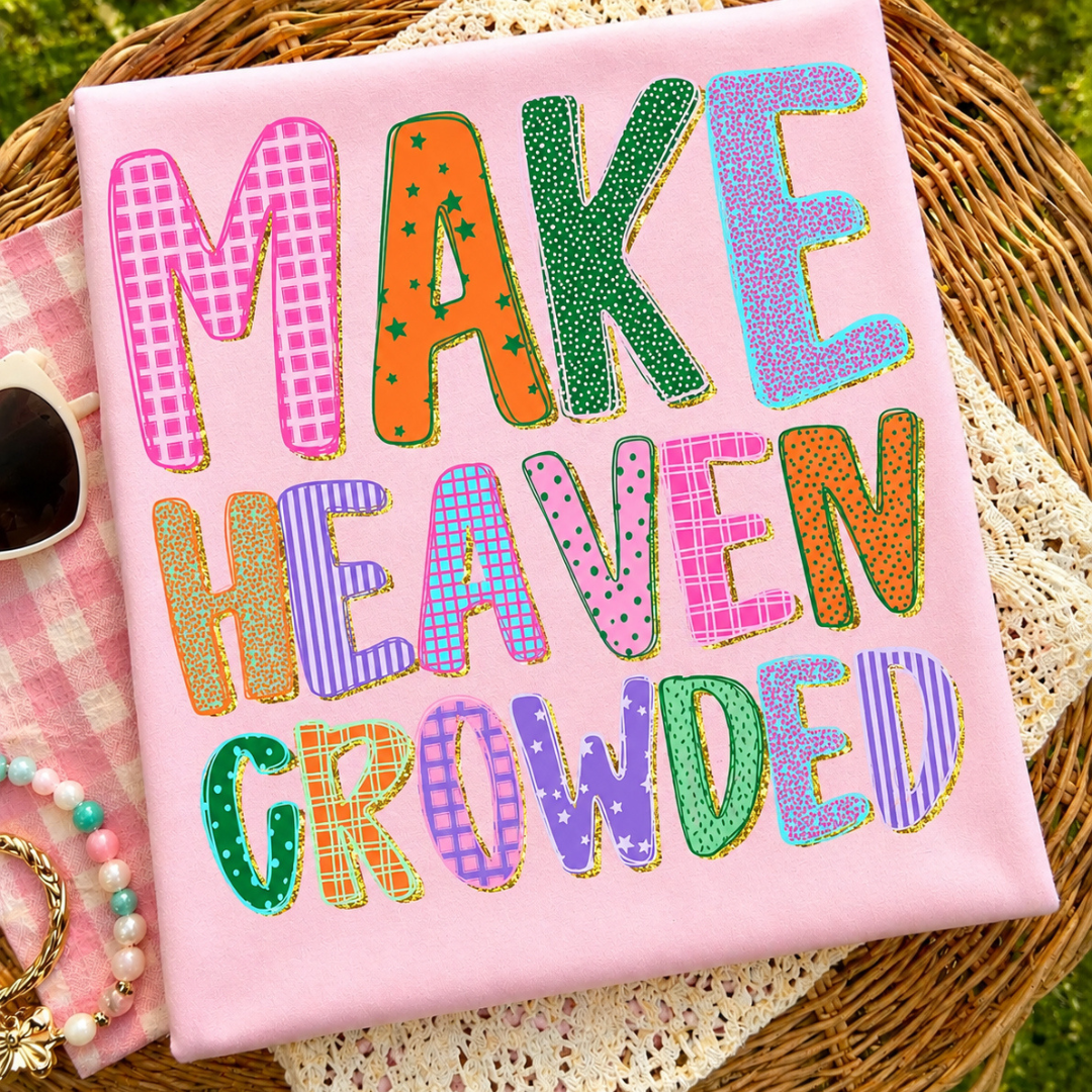 Light pink graphic tee featuring colorful patterned lettering that reads "Make Heaven Crowded."