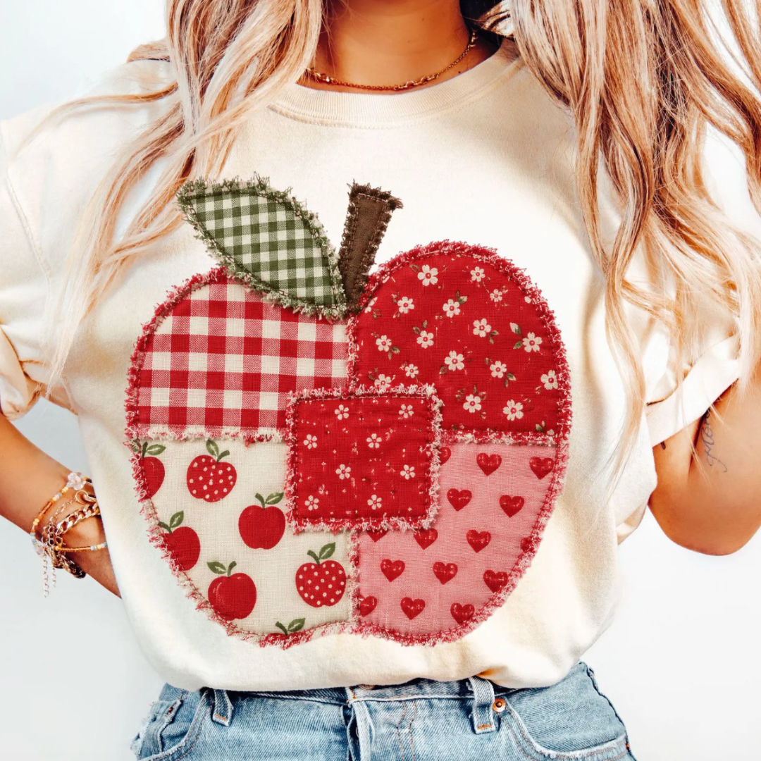 Natural graphic tee featuring a vintage-inspired patchwork apple with gingham, floral, heart, and apple-print fabrics in a faux appliqué design.