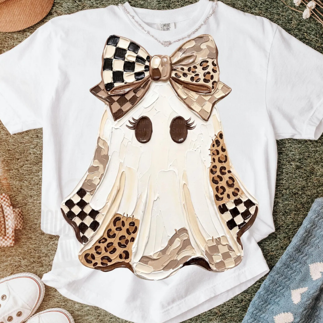 White graphic tee featuring a cute ghost with long eyelashes and a large bow in checkerboard, leopard, and neutral prints with hand-painted inspired artwork.