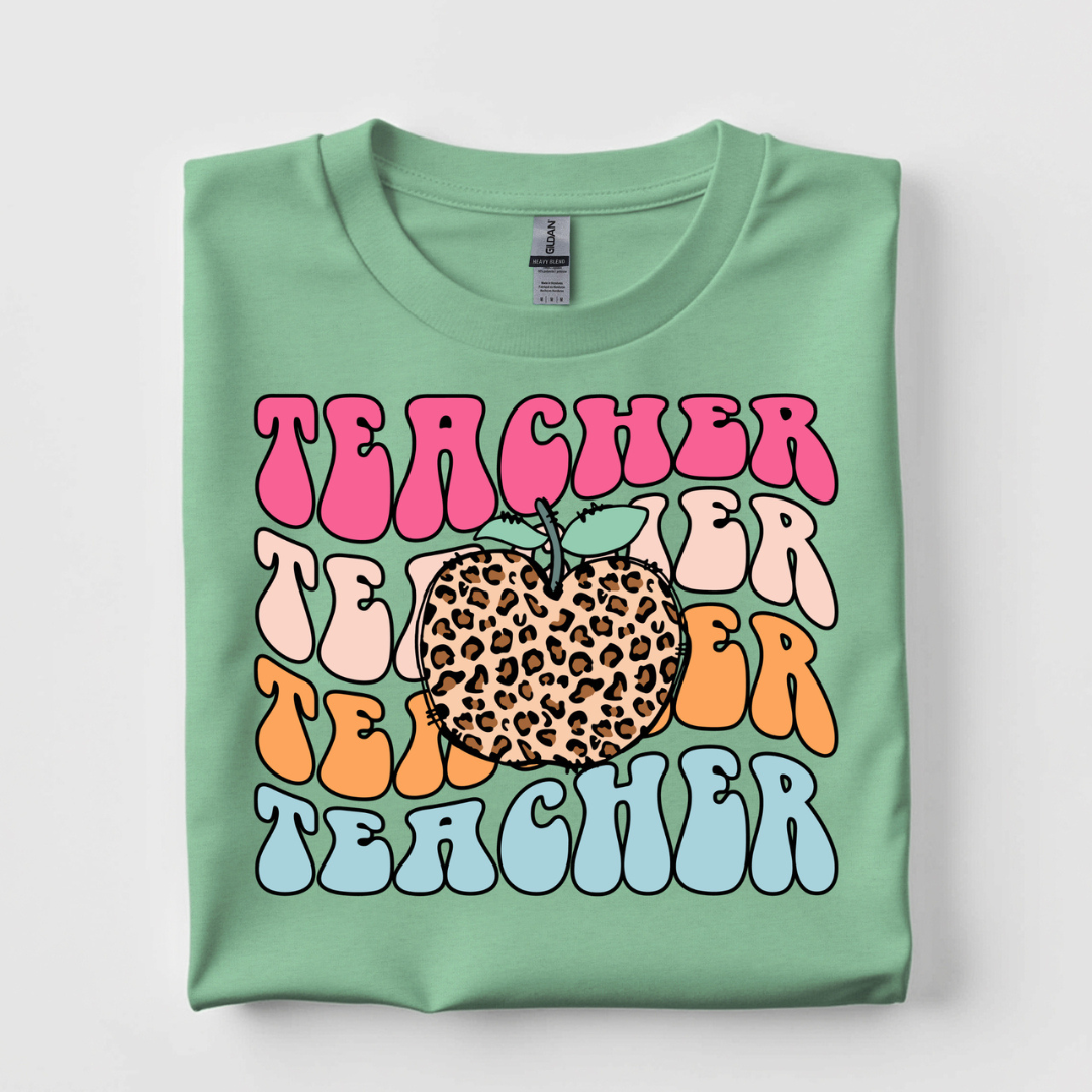Mint green graphic tee featuring repeating colorful Teacher lettering with a leopard print apple in the center.