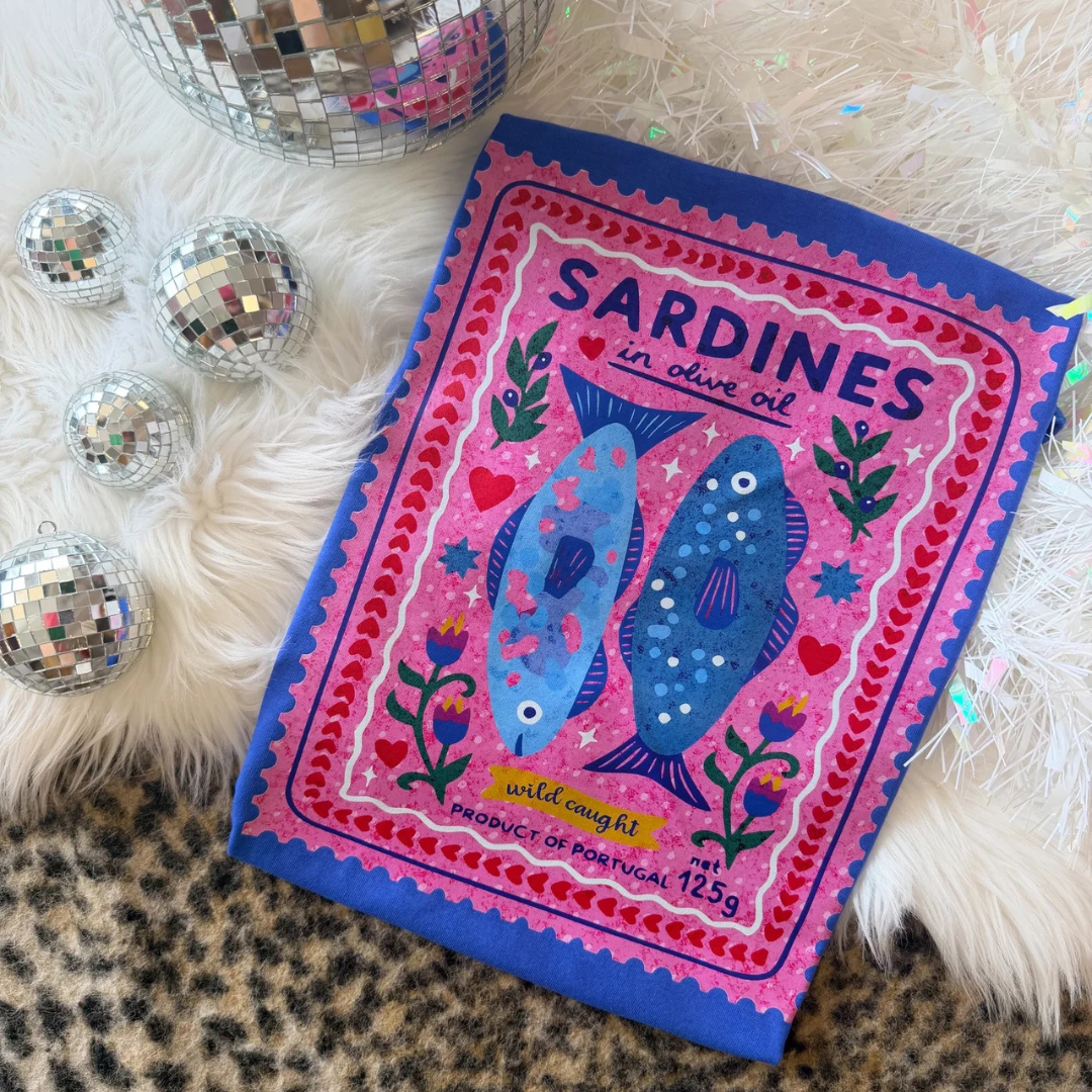 Royal blue graphic tee featuring a colorful vintage Portuguese sardine tin illustration with whimsical florals, hearts, and coastal-inspired artwork.