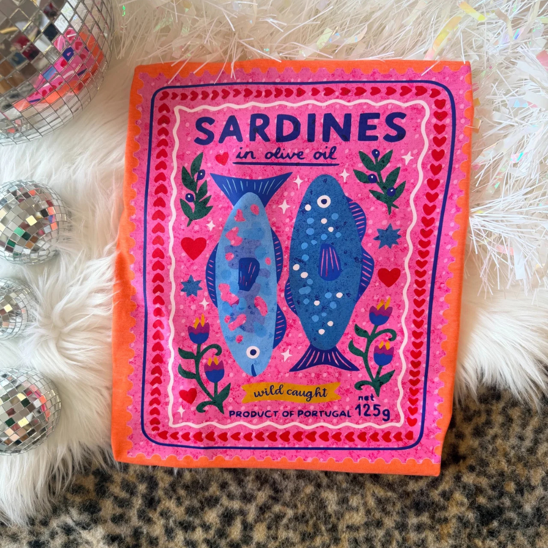 Bright orange graphic tee featuring a colorful vintage Portuguese sardine tin illustration with whimsical florals, hearts, and coastal-inspired artwork.
