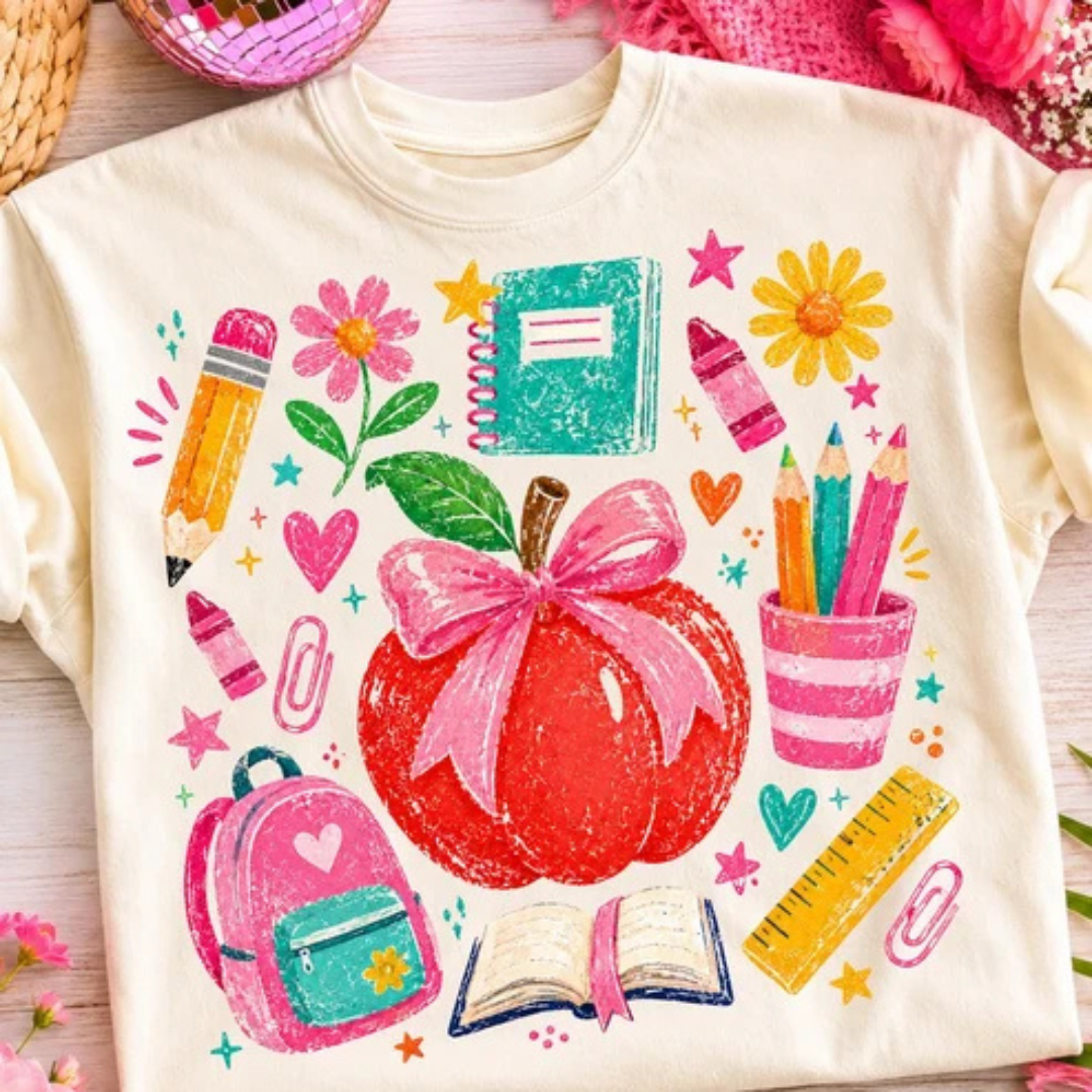 Natural graphic teacher tee featuring a pink bow apple surrounded by colorful school supplies including pencils, notebooks, flowers, backpack, ruler, crayons, and classroom icons.