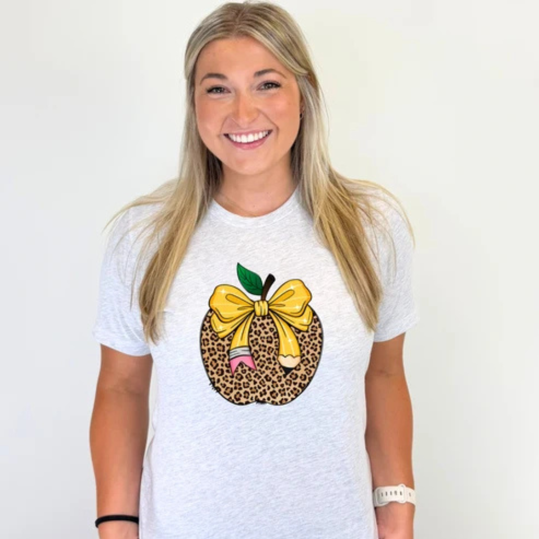 Ash grey graphic teacher tee featuring a leopard print apple with a yellow bow and pencil ribbon, perfect for back-to-school and everyday classroom wear.