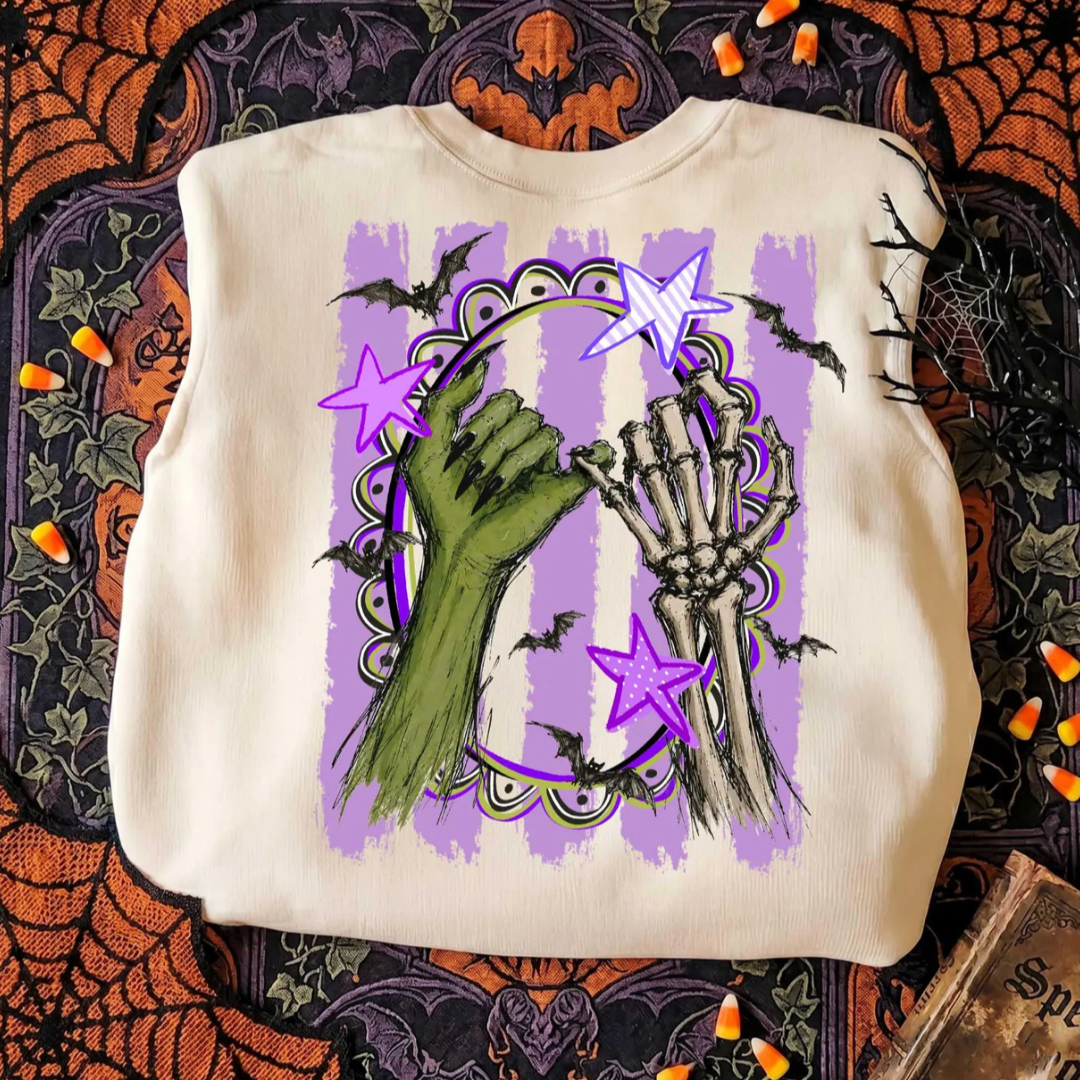 Natural Halloween graphic tee featuring a green witch hand and skeleton hand making a pinky promise with lavender stripes, bats, and spooky accents.