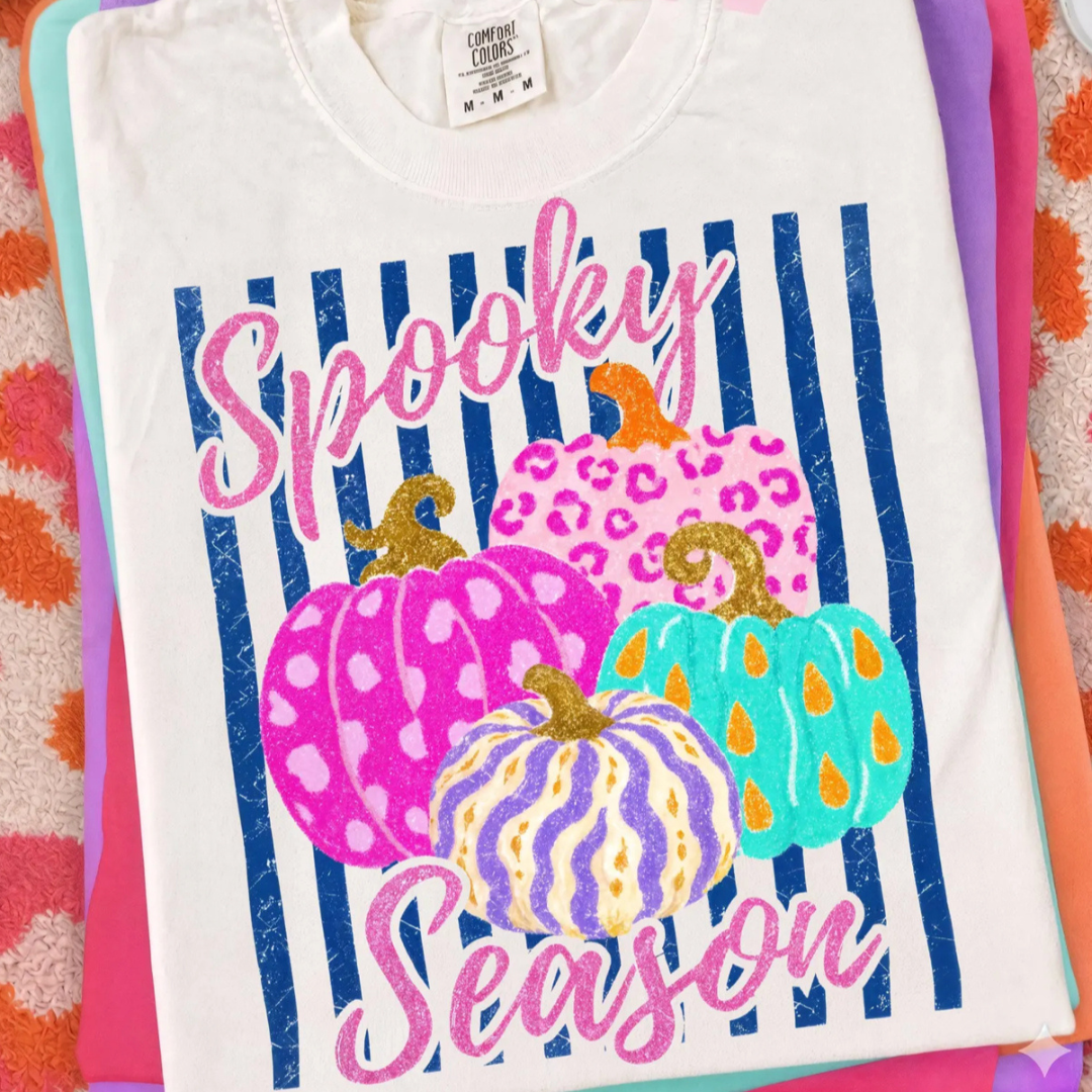 White graphic tee featuring colorful patterned pumpkins with navy stripes and glitter-inspired "Spooky Season" lettering.