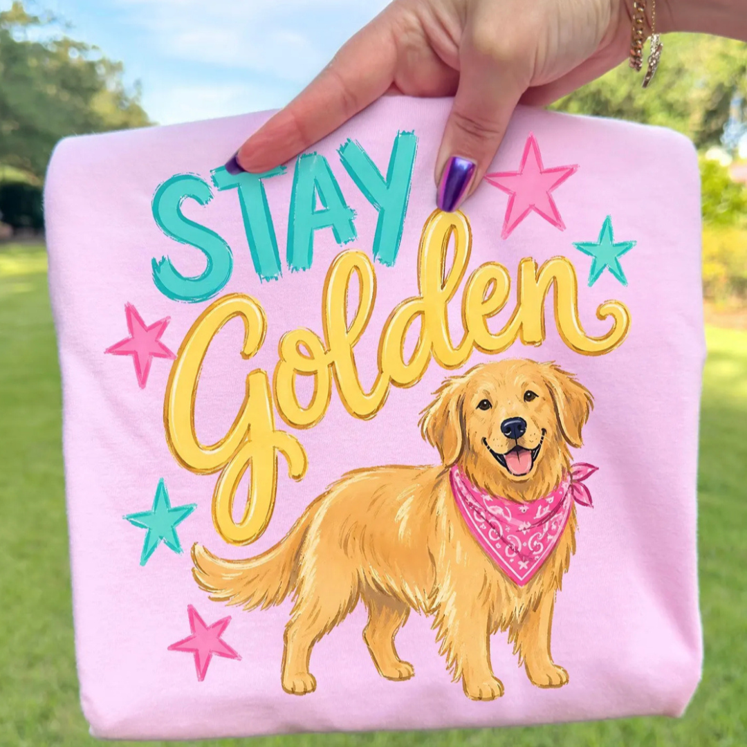 Light pink graphic tee featuring colorful Stay Golden lettering, star accents, and a Golden Retriever wearing a pink bandana.