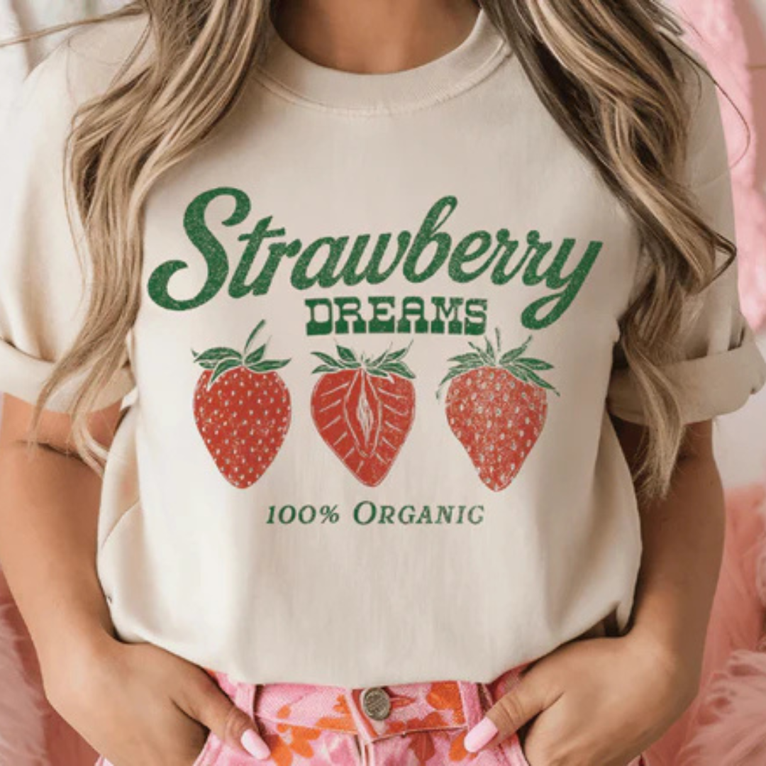 Cream graphic tee featuring a Strawberry Dreams design with vintage-style strawberries, green lettering, and 100% Organic text.