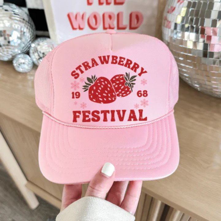 Pink and cream foam trucker hat featuring a Strawberry Festival graphic with strawberries, floral accents, and vintage-inspired lettering.