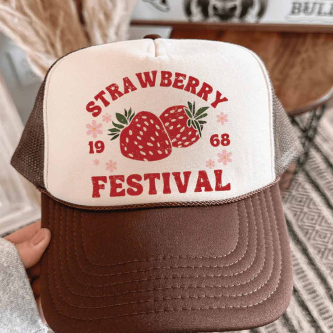 Pink and cream foam trucker hat featuring a Strawberry Festival graphic with strawberries, floral accents, and vintage-inspired lettering.