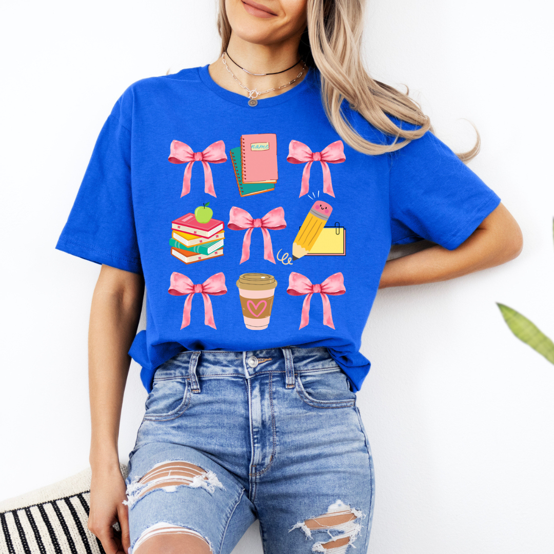 Royal blue teacher graphic tee featuring pink bows, notebooks, stacked books, a pencil, and a coffee cup.