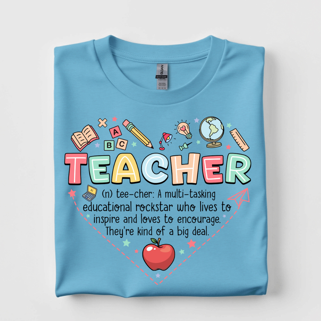 Sky blue graphic tee featuring a colorful Teacher definition graphic with books, globe, pencil, apple, and classroom icons.