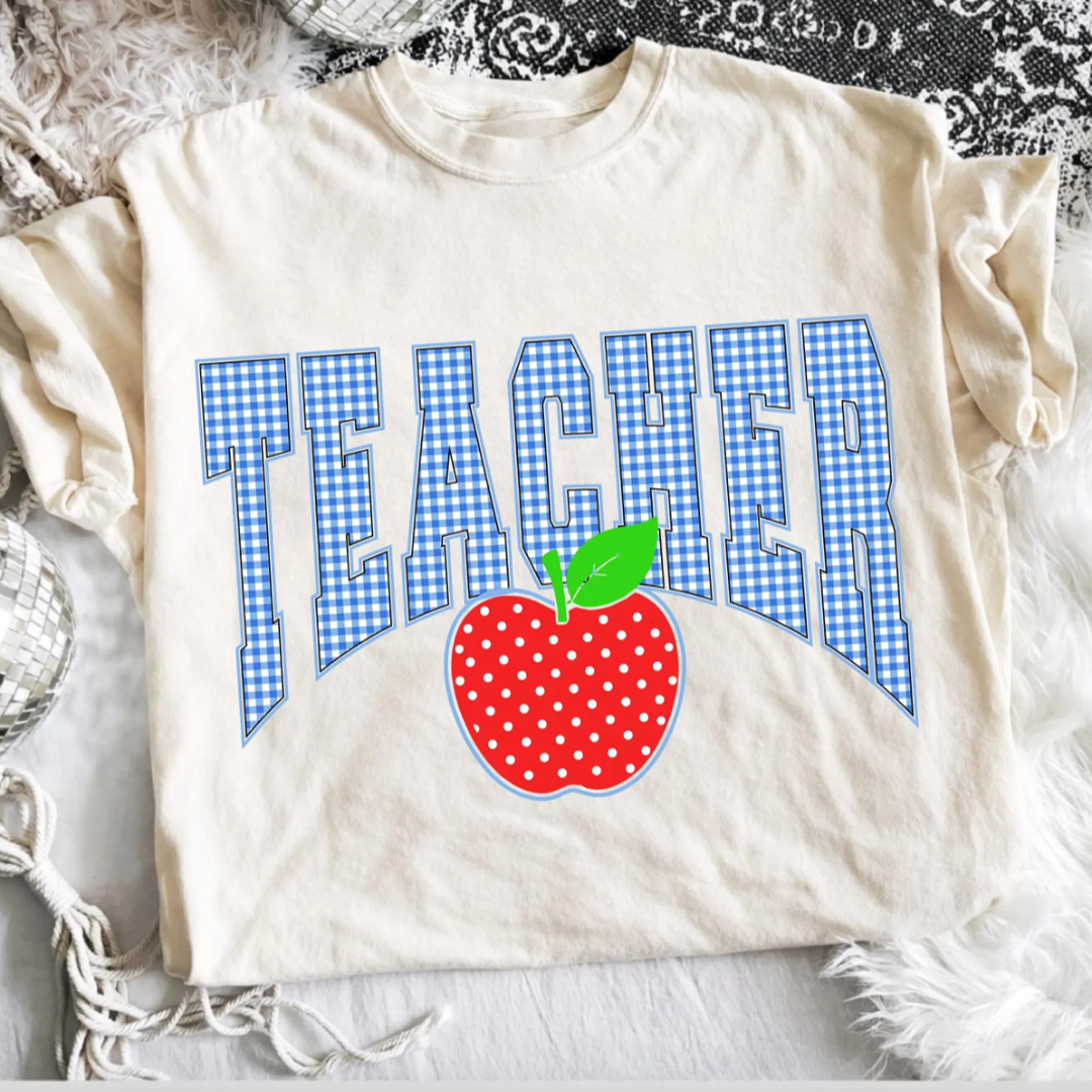 Natural beige teacher graphic tee featuring blue gingham varsity lettering with a red polka dot apple accent.