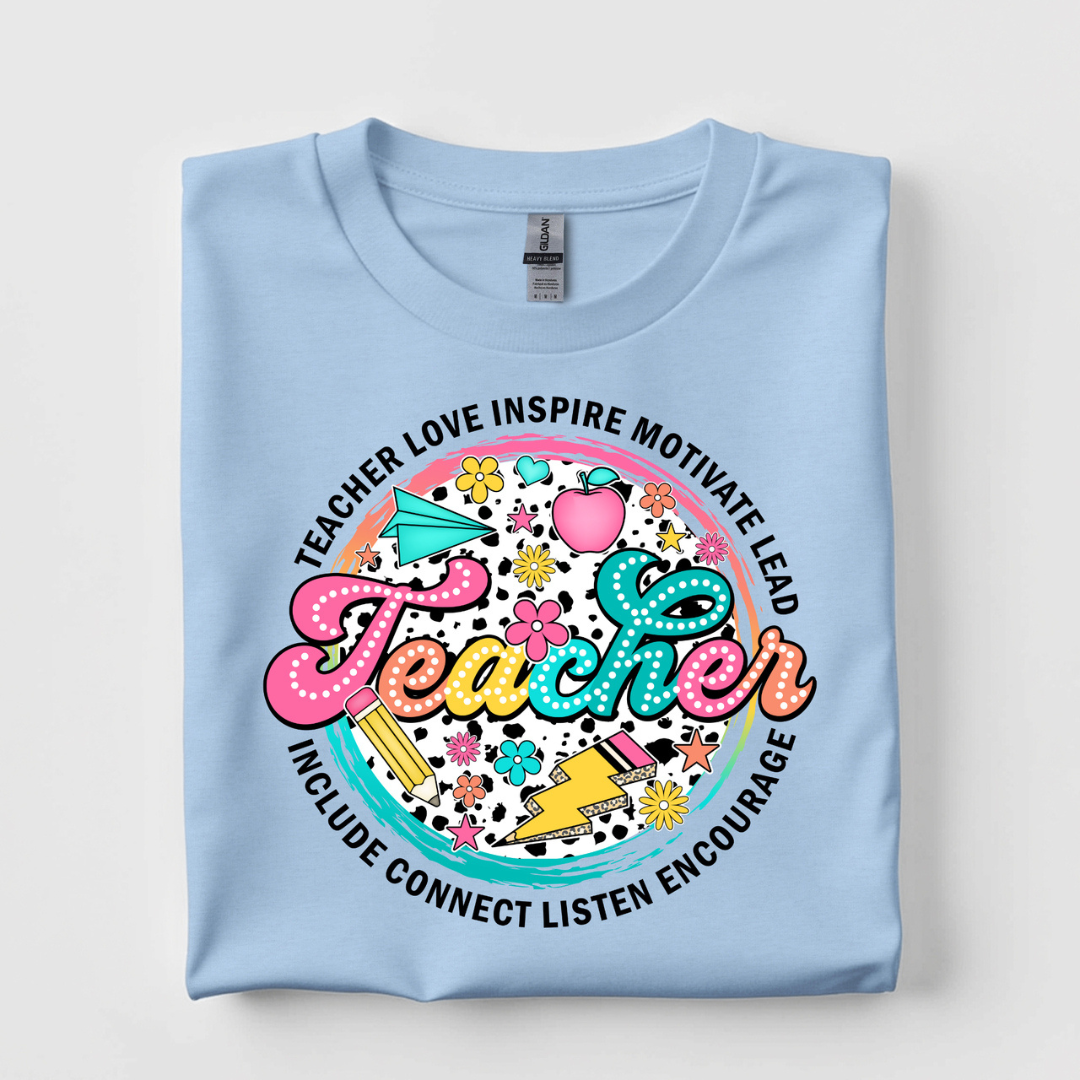 Light blue graphic tee featuring a colorful "Teacher" design surrounded by inspirational words and classroom-themed illustrations.