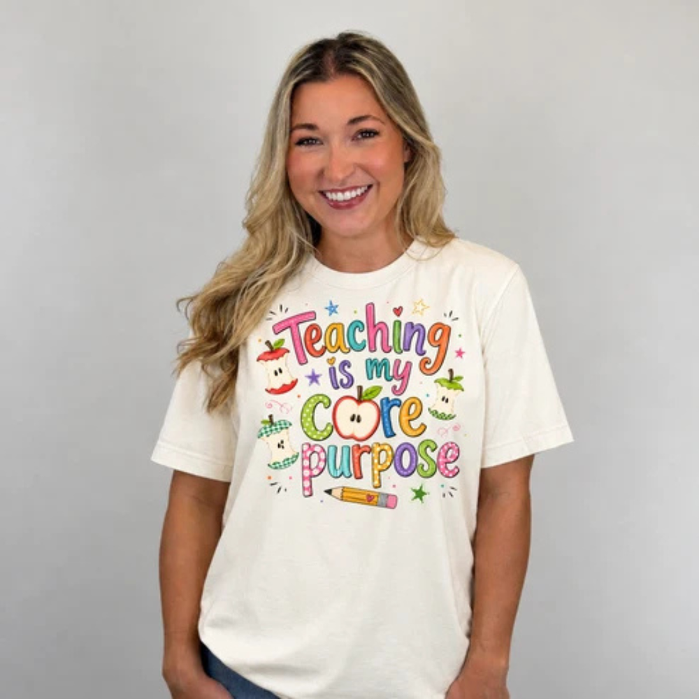 Natural graphic teacher tee featuring colorful "Teaching Is My Core Purpose" lettering with apple cores, a pencil, and classroom-inspired artwork.