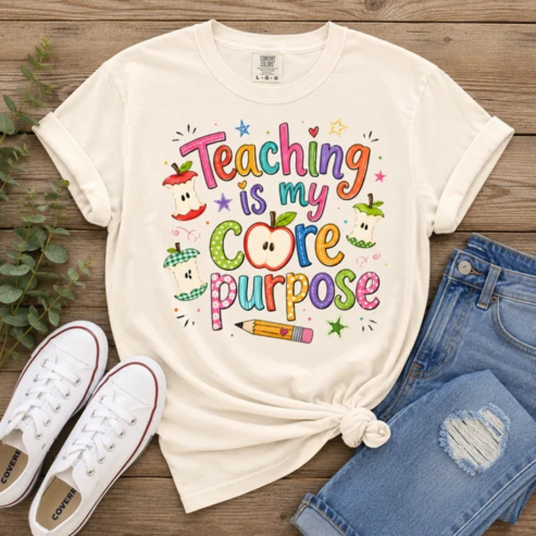 Natural graphic teacher tee featuring colorful "Teaching Is My Core Purpose" lettering with apple cores, a pencil, and classroom-inspired artwork.