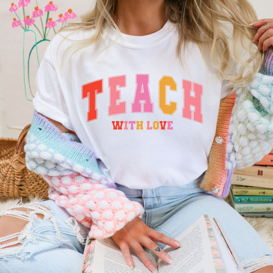White graphic teacher tee featuring colorful collegiate-style "Teach with Love" lettering.