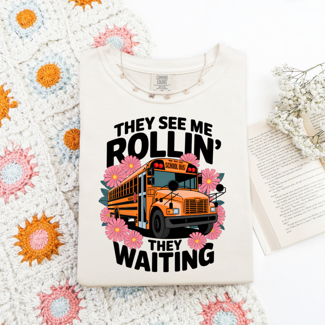 Ivory graphic tee featuring a yellow school bus with pink flowers and the phrase "They See Me Rollin', They Waiting."