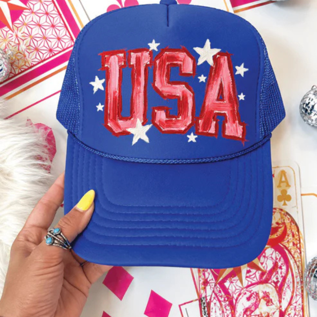 Royal blue foam trucker hat featuring oversized USA lettering with white star accents in a patriotic design.