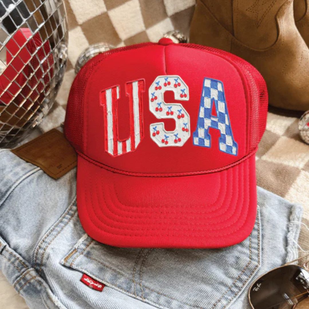 Red foam trucker hat featuring USA lettering with cherry and blue checkered patriotic accents.