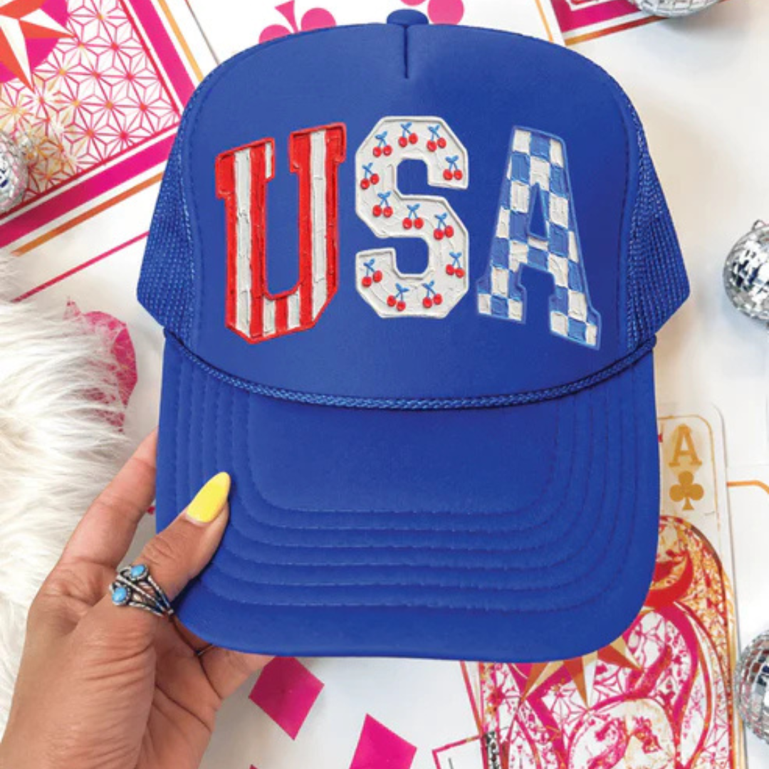 Royal blue foam trucker hat featuring USA lettering with cherry and blue checkered patriotic accents.