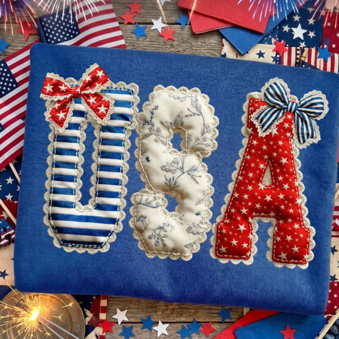 Royal blue graphic tee featuring patchwork-style USA letters with patriotic prints, bows, lace details, and red, white, and blue accents.