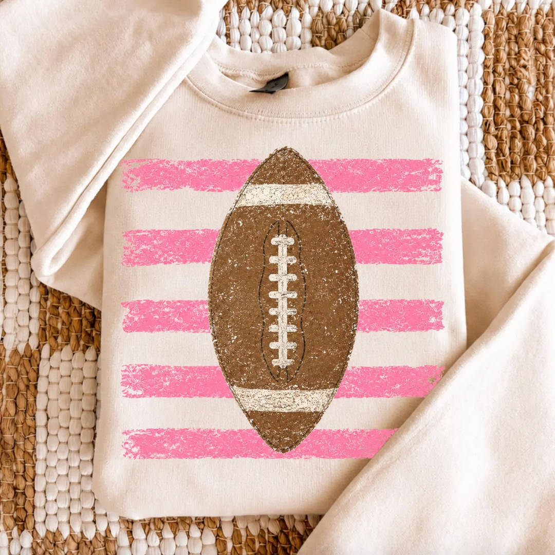 Natural graphic tee featuring a vintage distressed football over bold pink stripes for a feminine football game day look.