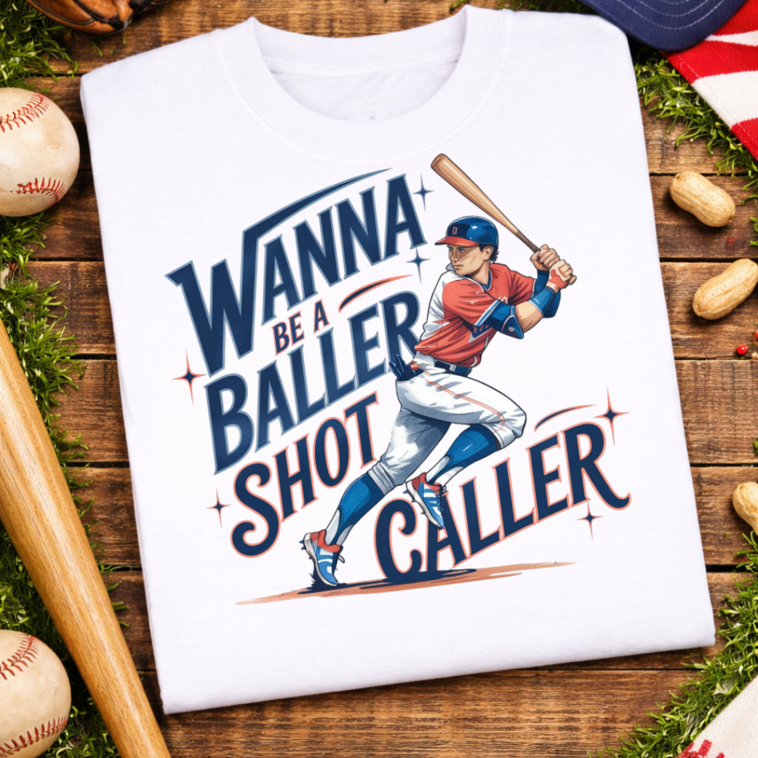 White graphic tee featuring a vintage-style baseball player with the phrase "Wanna Be a Baller, Shot Caller" in navy and red lettering.
